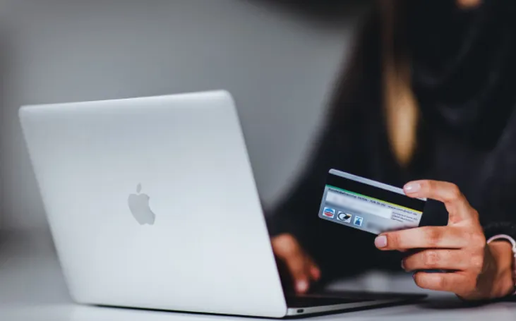 Person holding a payment card in front of a laptop